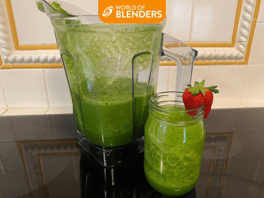 Spinach smoothie in blender next to glass jar of green smoothie with strawberry garnish