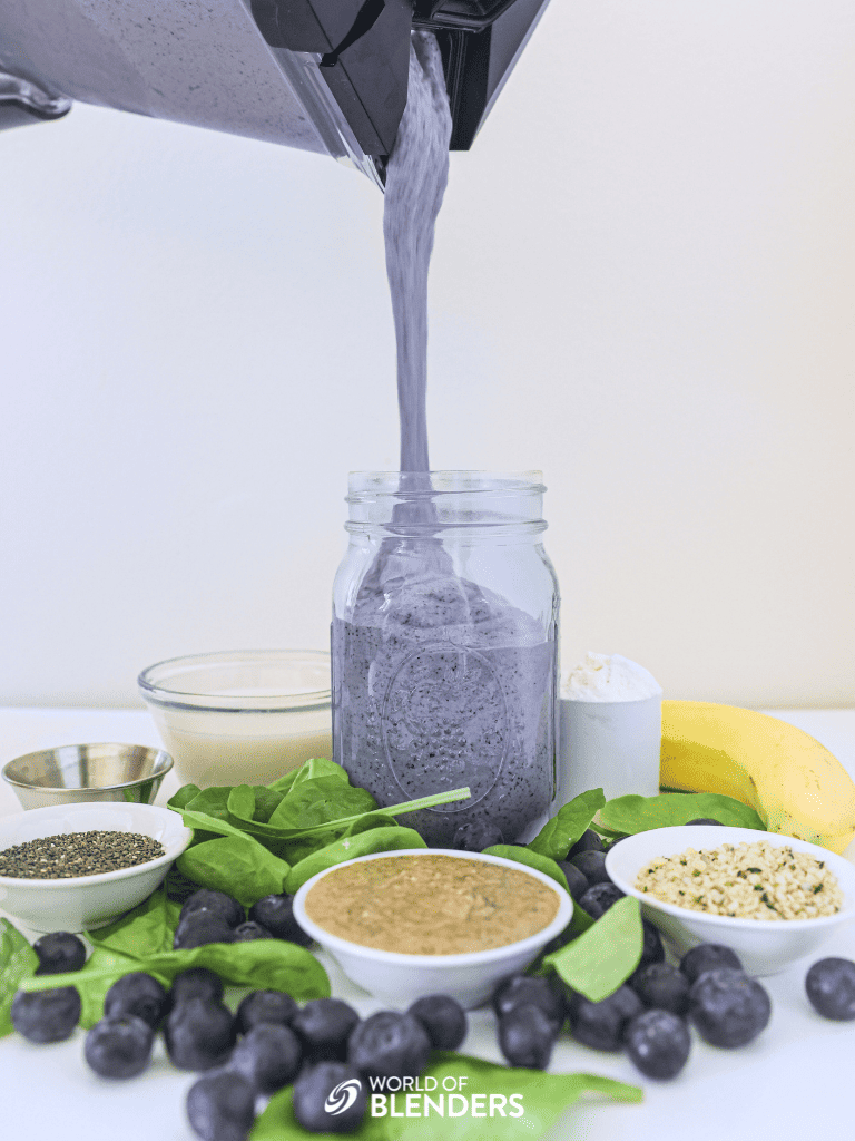 pouring a high protein green smoothie into a mason jar with smoothie ingredients around it 