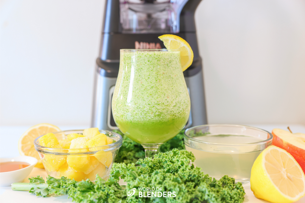 kale apple smoothie in a glass with kale and fruit around it and a ninja blender behind it