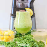 kale apple smoothie in a glass with kale and fruit around it and a ninja blender behind it