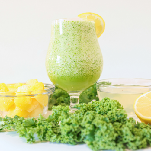 kale apple smoothie in a glass with kale and fruit around it