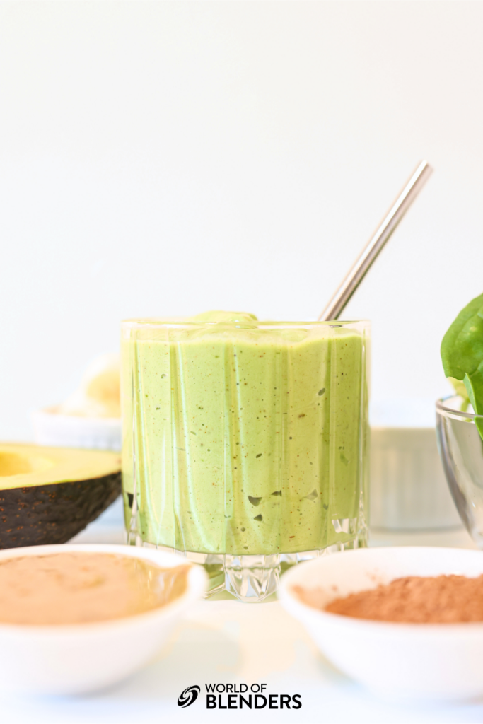spinach avocado smoothie in a short glass with ingredients around it