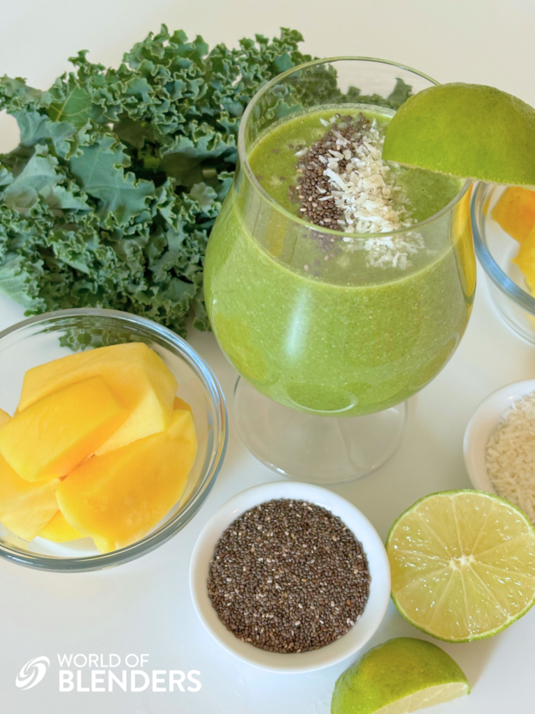 healthy mango kale smoothie in a glass with a lime wedge and ingredients around it